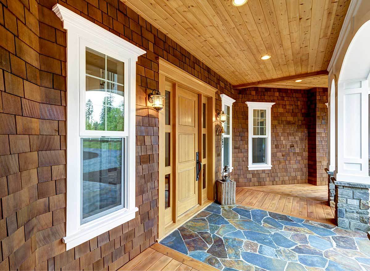 Covered porch with wood plank ceiling and a wooden entry door adorned with sidelights.