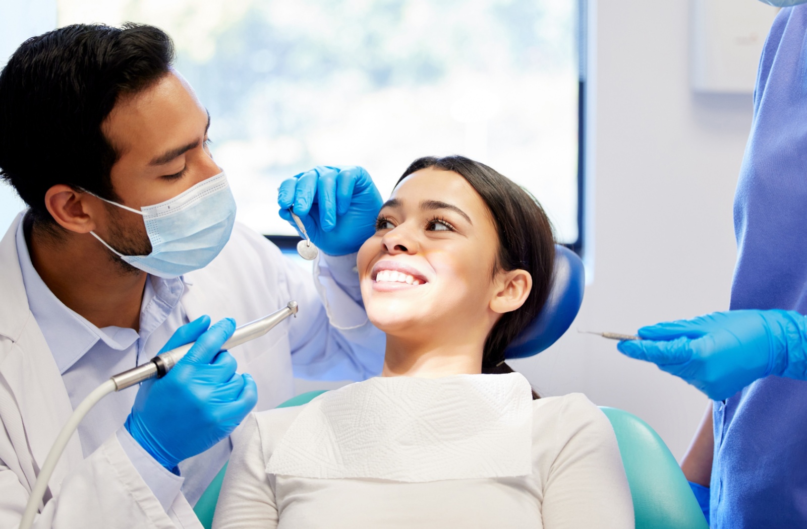 A dentist examining a smiling patient in the dental chair to check for cavities during a routine checkup.