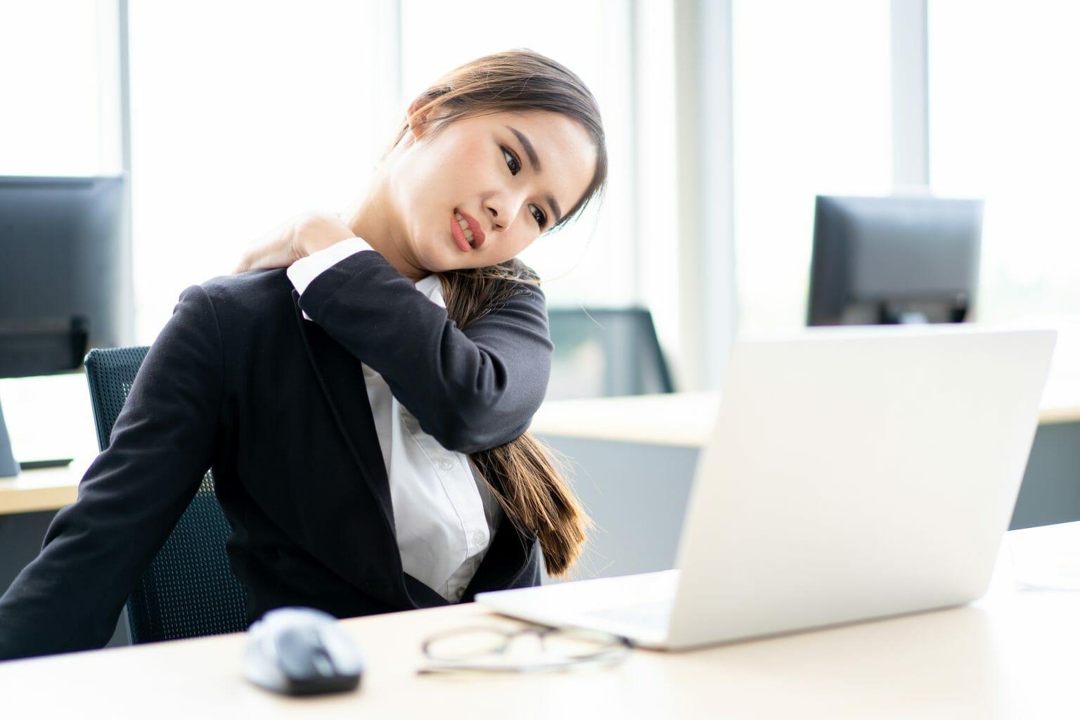 A person sitting at a desk with her arm around her neck

Description automatically generated