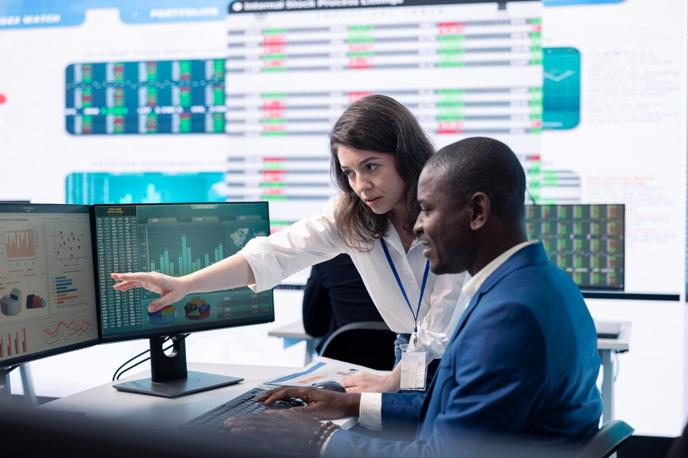 Two people in an office analyzing data on monitors.