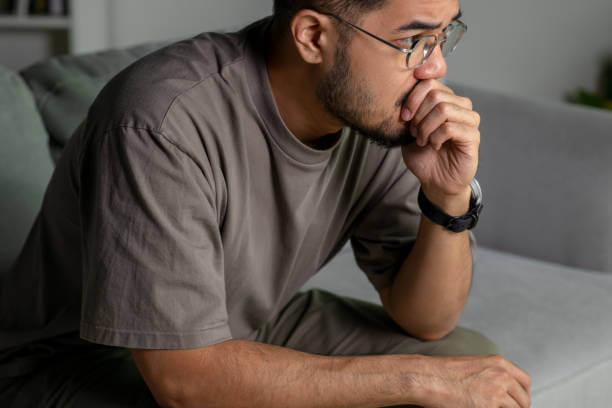 A worried man sitting on a couch with a stressed expression, representing anxiety and mental strain.