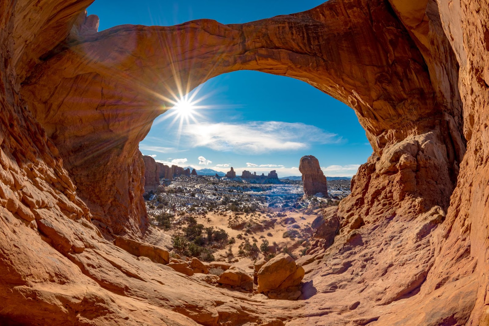 Panoramic view looking out from under a natural arch onto the desert valley in front where other sandstone rock formations are visible