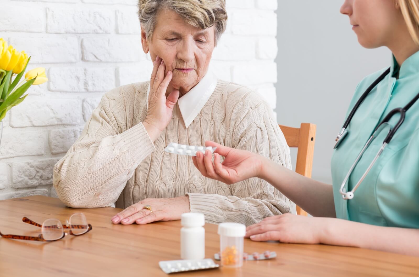 A staff member handing an older adult in memory care a blister pill pack.