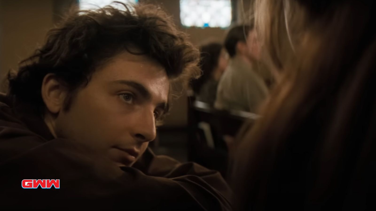 Bob Dylan with curly hair looks attentively towards someone in a dim room.