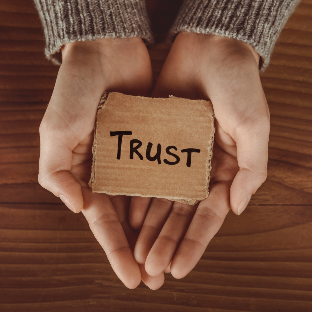 Hands holding a small piece of cardboard with the word 'trust' on it