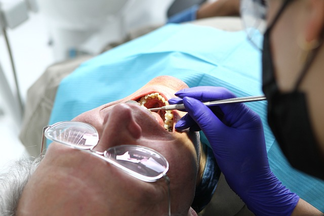 A man undergoing a dental check-up by a dentist, with tools and equipment in a clinic setting.