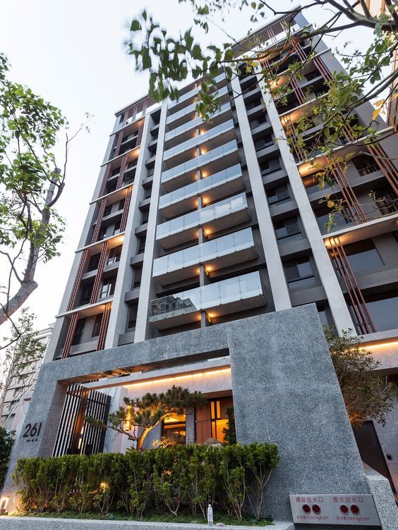 Gedung apartemen modern bertingkat tinggi dengan balkon kaca dan pencahayaan hangat, dilihat dari bawah dengan sudut pandang perspektif. 