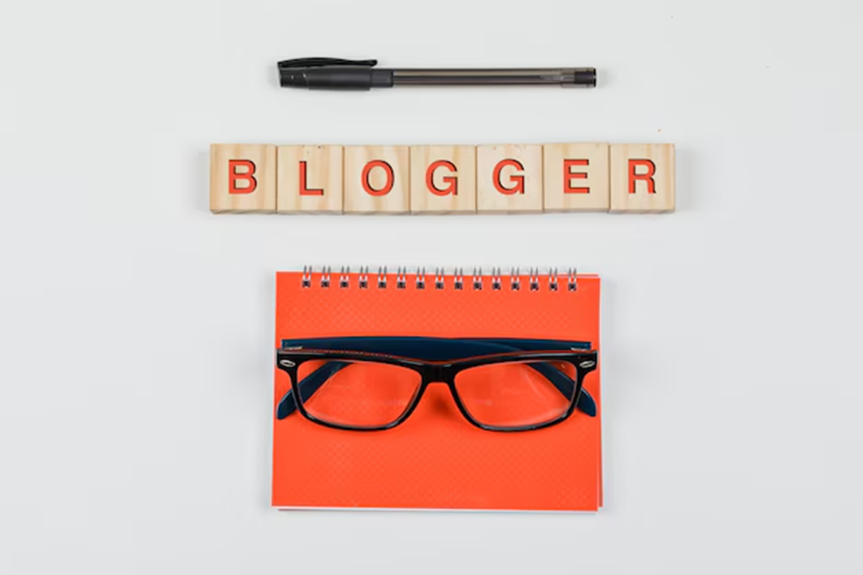 A pen, notebook, pair of glasses, and blocks with the word "blogger"