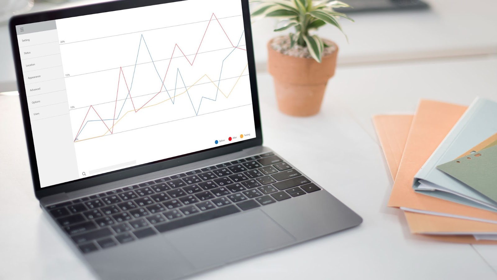 Laptop with data on the screen with a potted plant and folders in the background. 