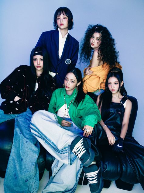 This may contain: four young women sitting next to each other in front of a blue wall, one wearing a green jacket