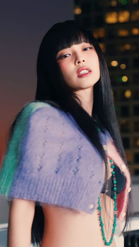 This contains an image of BLACKPINK Jennie with long black hair wearing a blue and green top in front of a cityscape