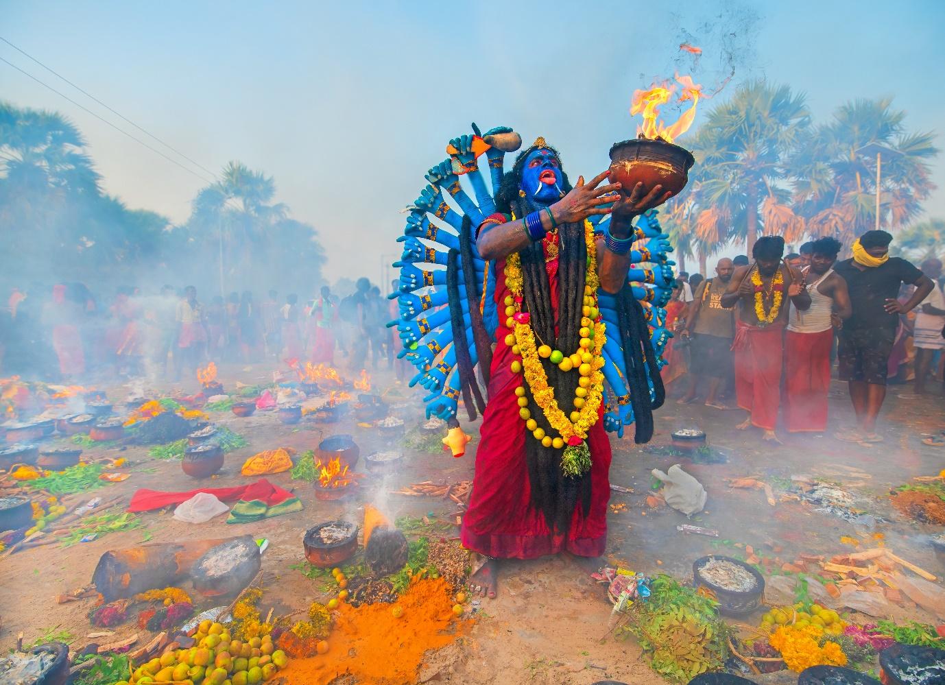 A person with blue face and blue paint holding a bowl of fire

Description automatically generated