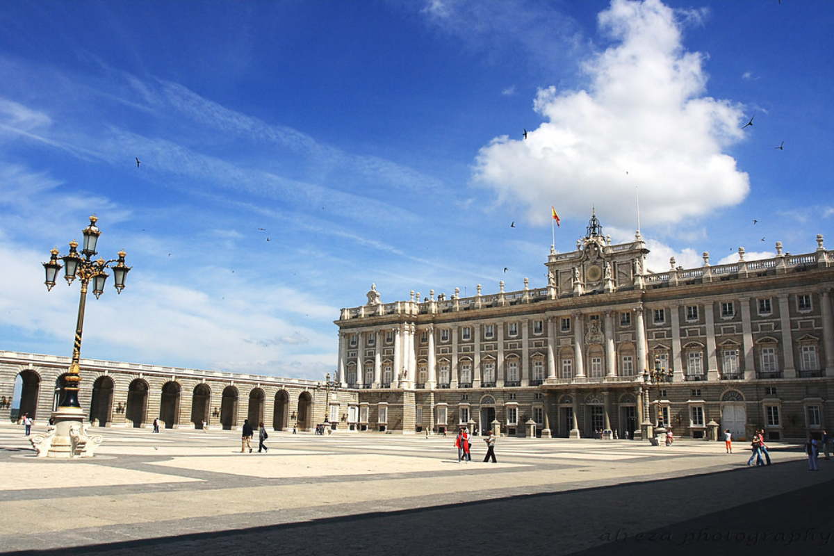 A white old style building wide in size and people viewing it's structure