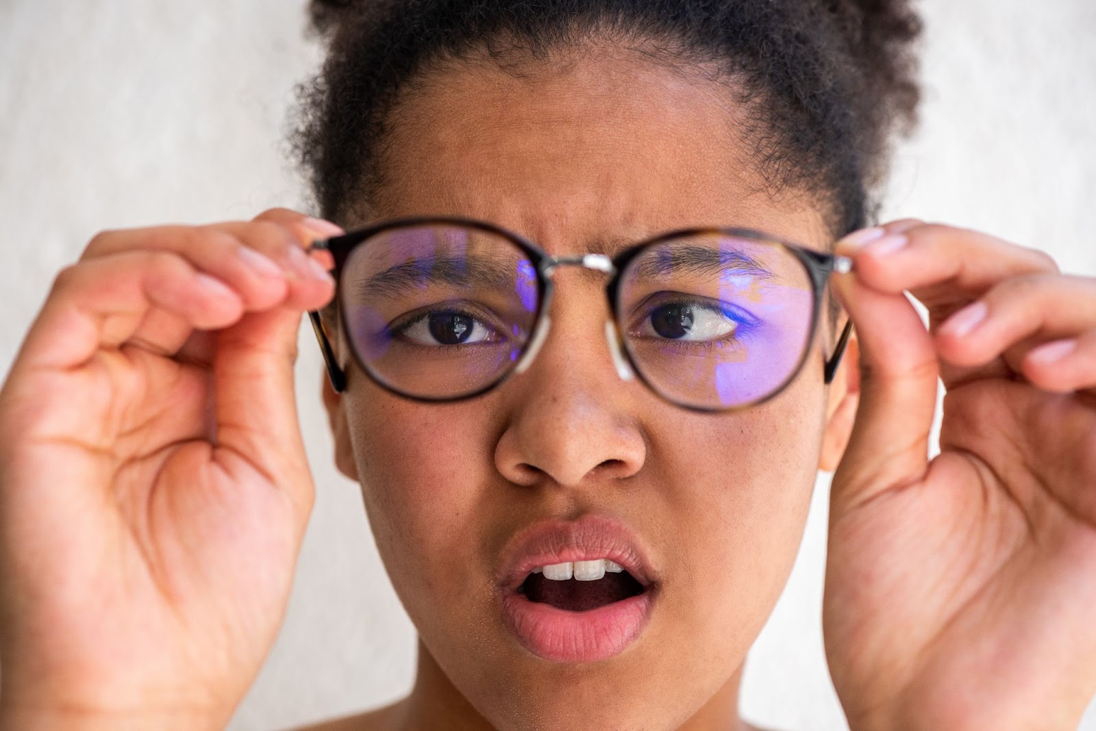 A young girl holding glasses in front of her eyes to treat crossed eyes.
