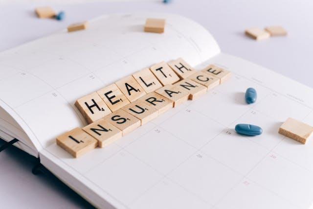 Wooden blocks spelling “health insurance” in a white notebook. 