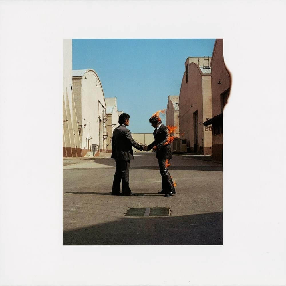 Pink Floyd's 'Wish You Were Here' album cover featuring two men shaking hands, with one of them on fire, set in an industrial lot.