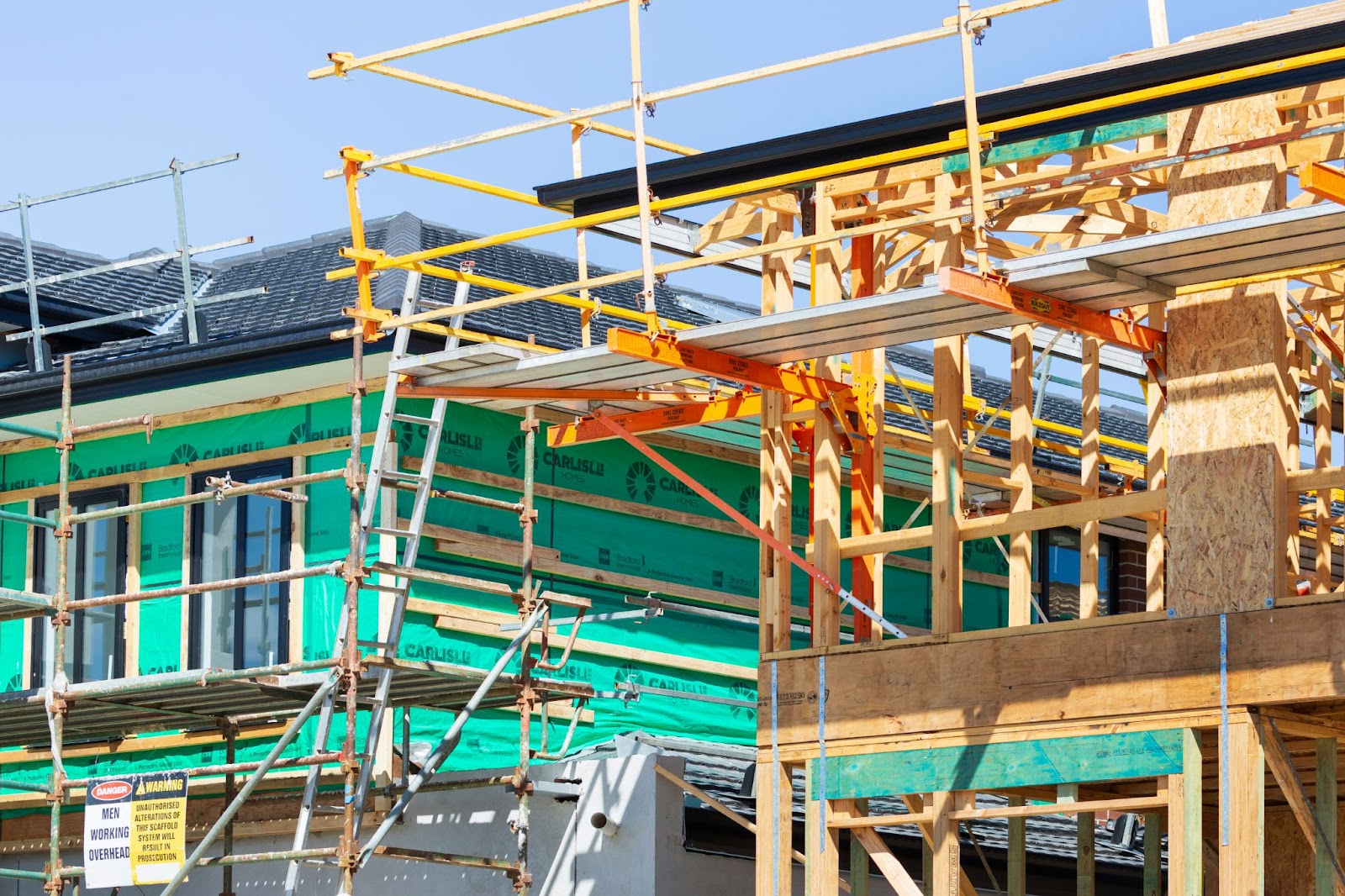 Image of a new housing development being build. Wood framed buildings with scaffolding and ladders.