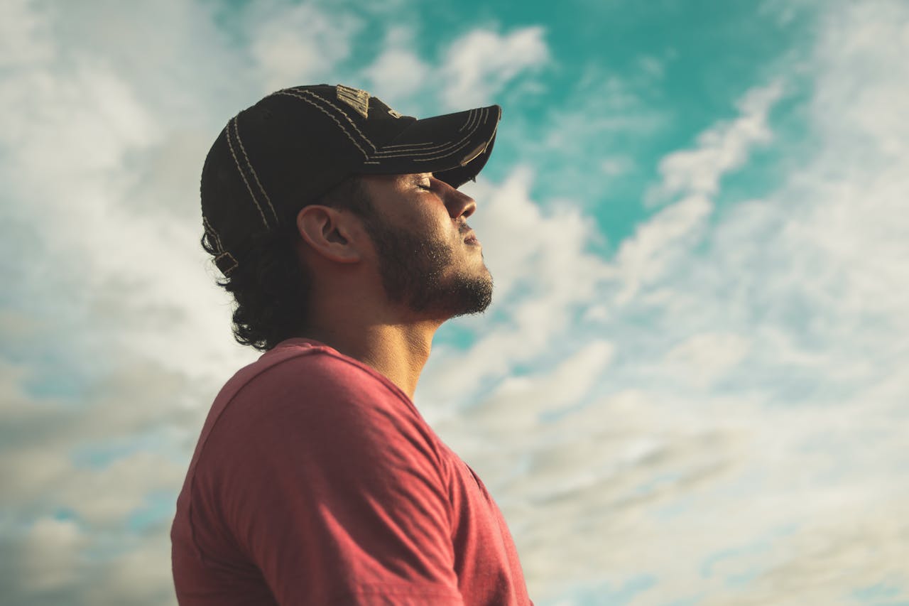 A man wearing a baseball cap looks up, his face reflecting curiosity as he gazes at the sky above.