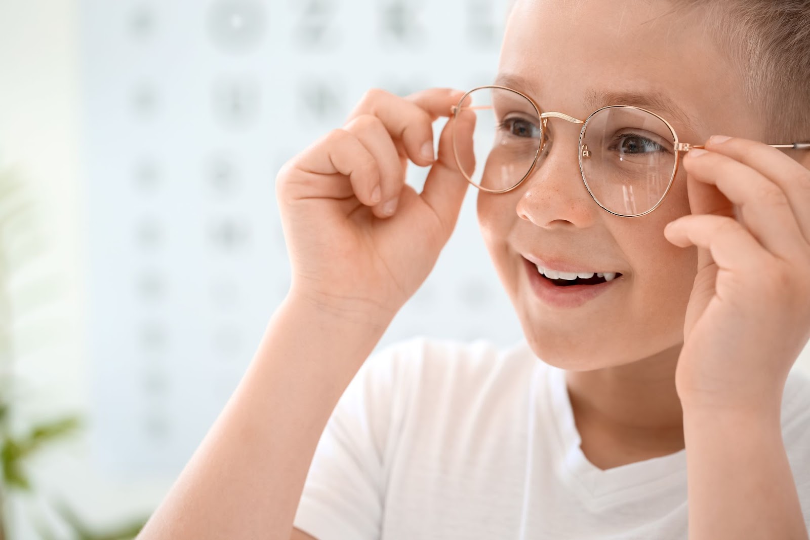 A smiling boy seeing clearly with glasses on and holding them with both hands.