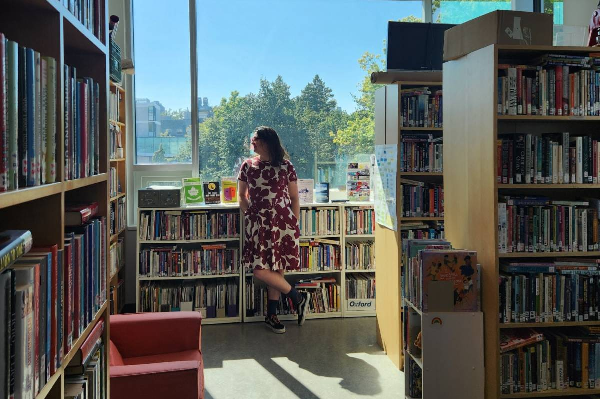 A femme person stands in front of low bookshelves with more book cases in rows in front of them