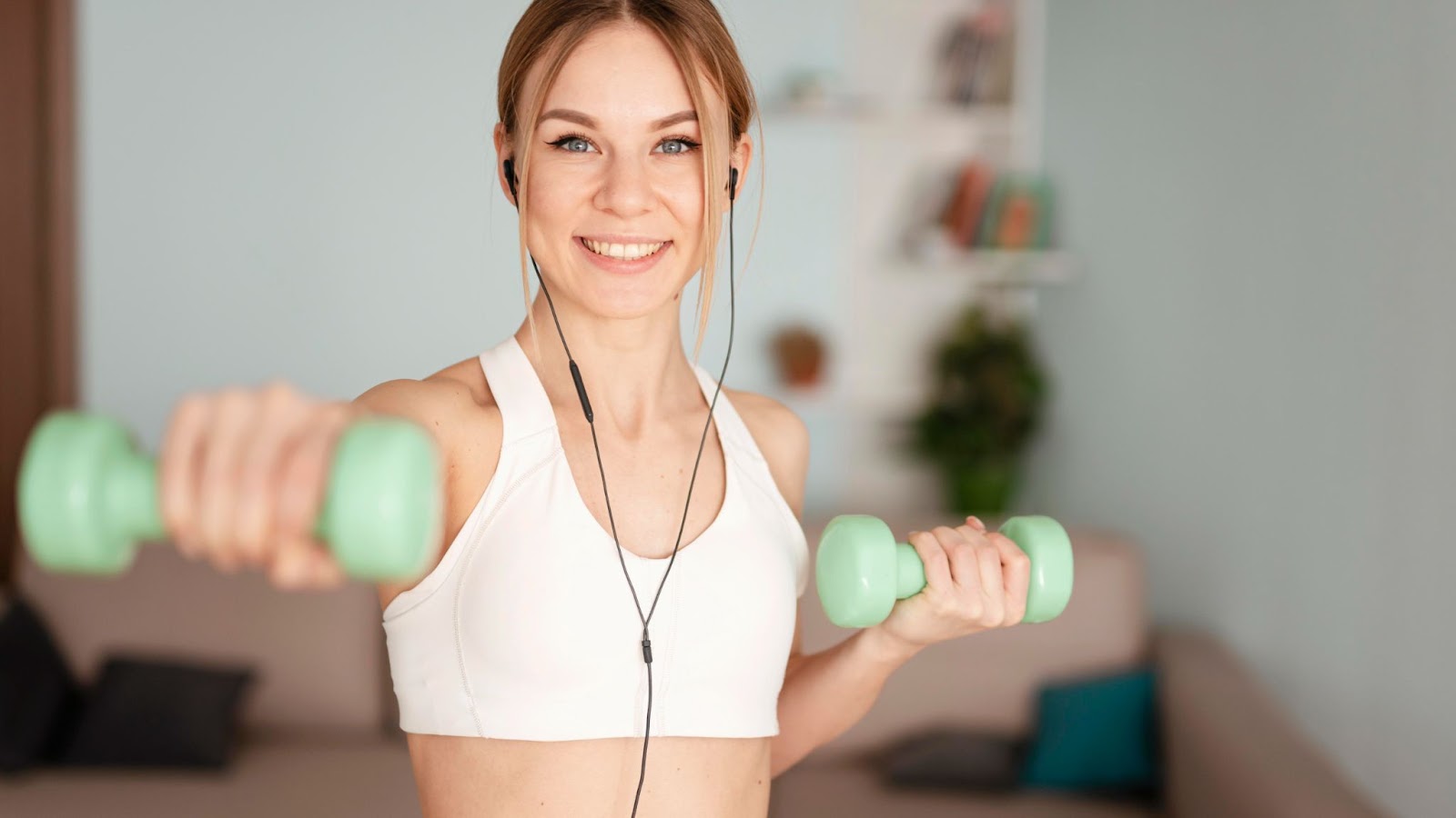 A woman in workout clothes lifts hand weights at home.