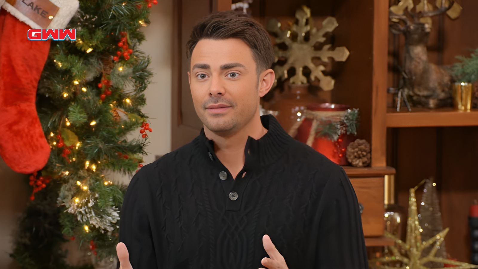 Jonathan Bennett in a black sweater speaks with a festive Christmas backdrop.