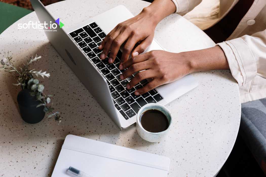 Hands typing on a laptop with a coffee cup and notebook nearby