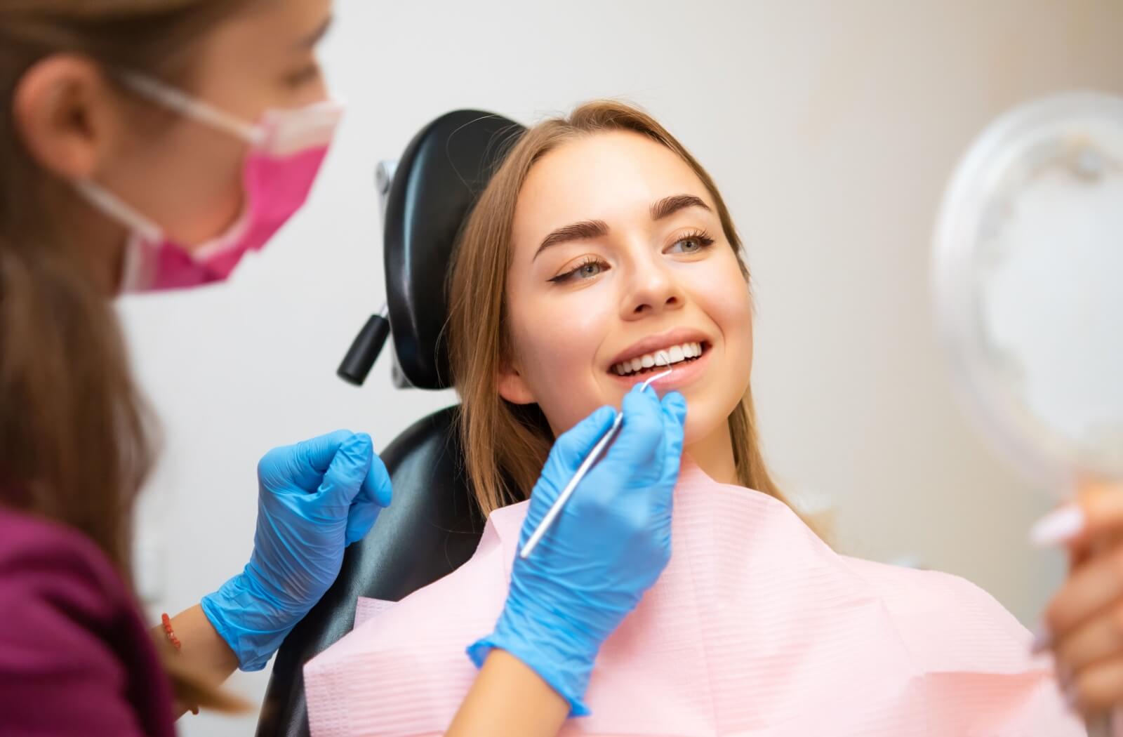 a dentist professionally cleans a patient's teeth to eliminate plaque and tartar while the patient holds a small mirror to observe their cleaner, healthier smile.