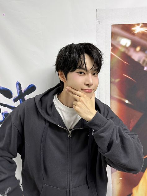 This contain Doyoung in front of a poster with his hand on his chin and looking at the camera