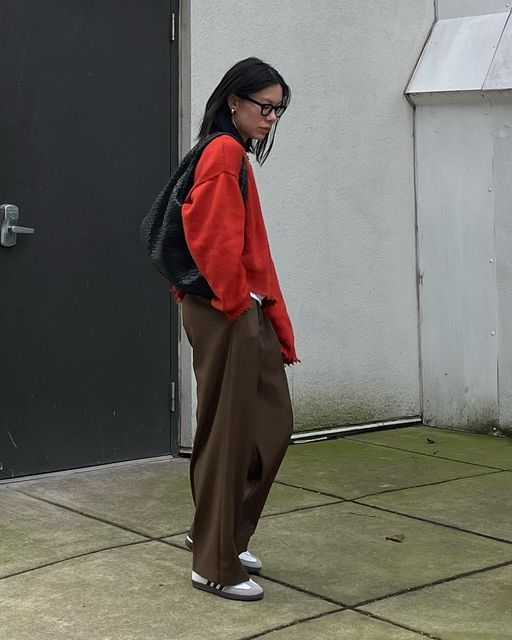 seorang wanita memakai celana cokelat, atasan merah, kacamata, dan tas hitam