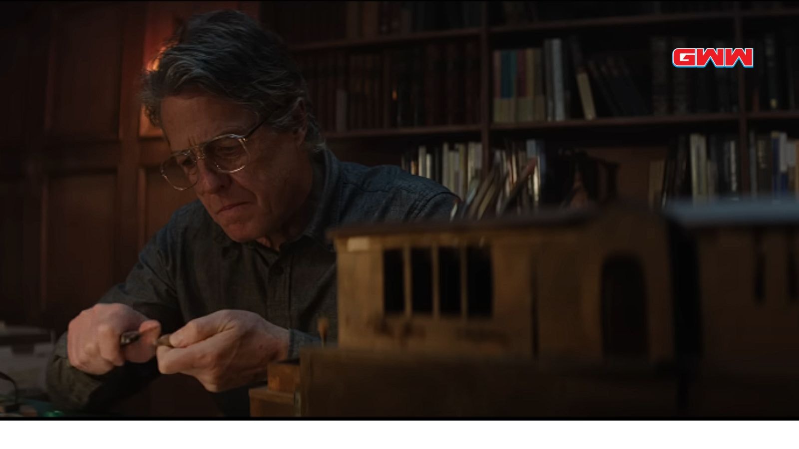 Hugh Grant working intently on a small model at a desk.