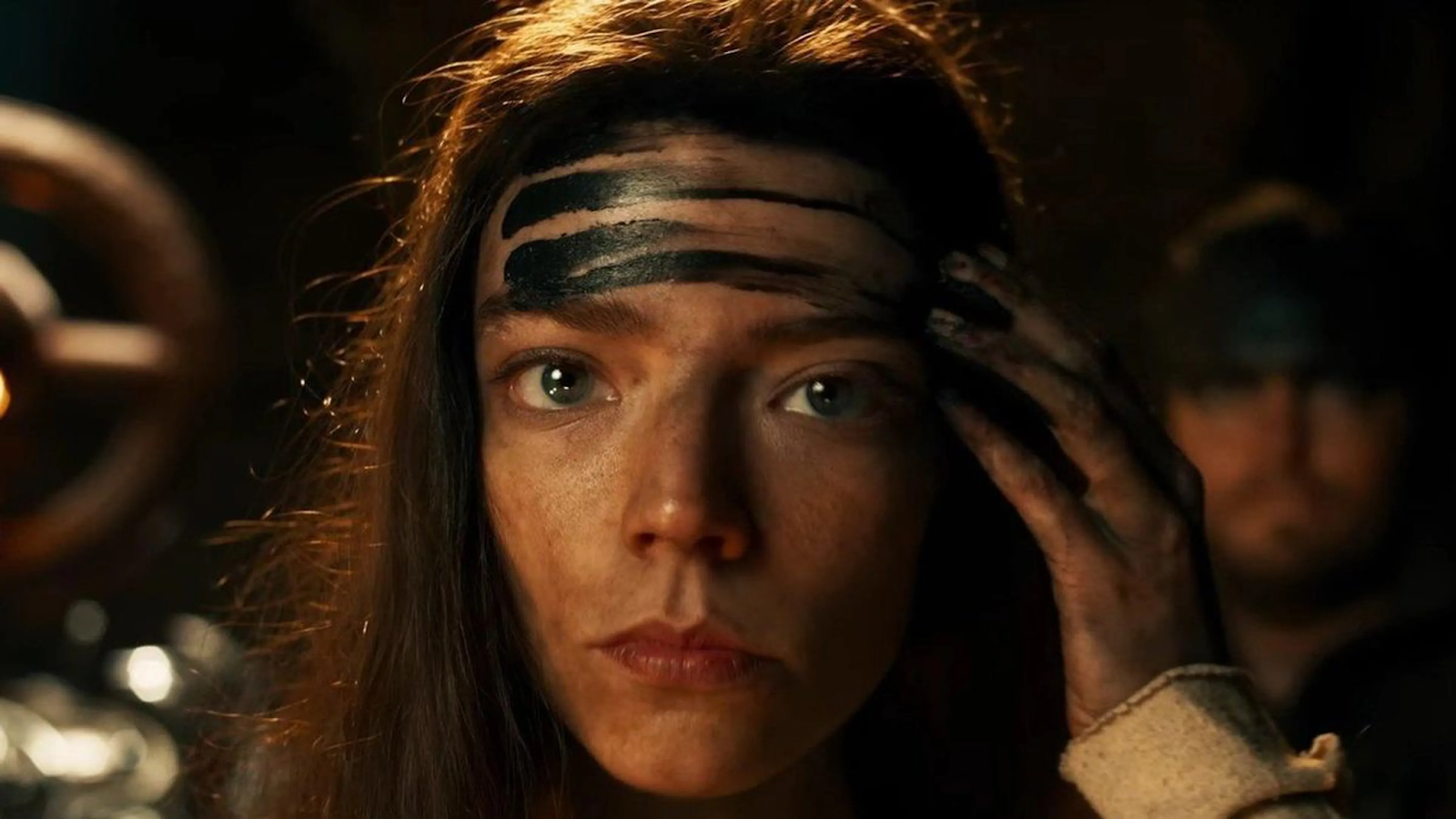 Primer plano de Anya Taylor-Joy como Furiosa, con su rostro manchado por marcas negras en medio de un ambiente postapocalíptico oscuro.