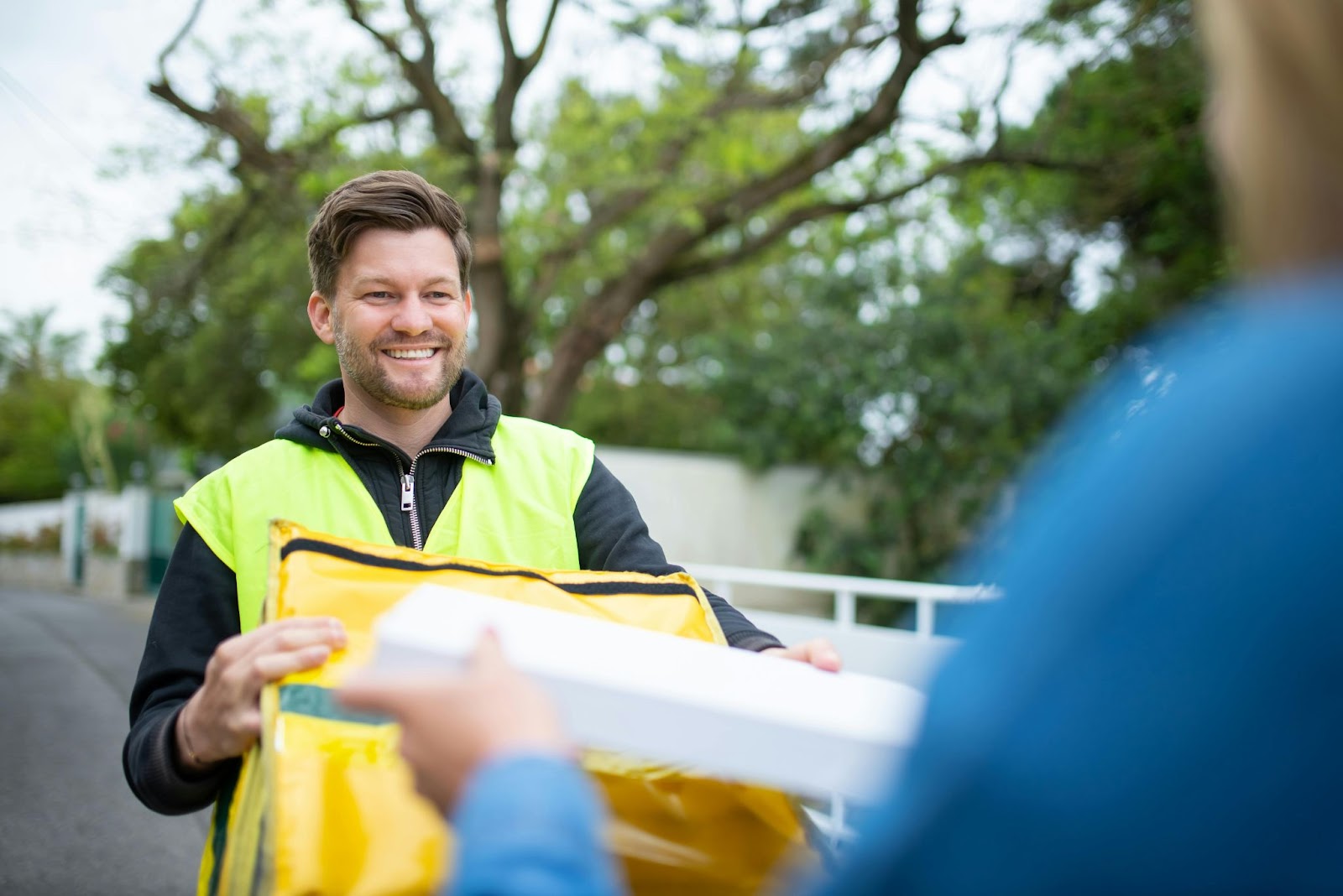 Hombre sonriendo mientras sostiene un paquete amarillo y recibe una hoja de papel, ilustrando un proceso de trazabilidad y gestión de transporte (TMS) en la última milla.