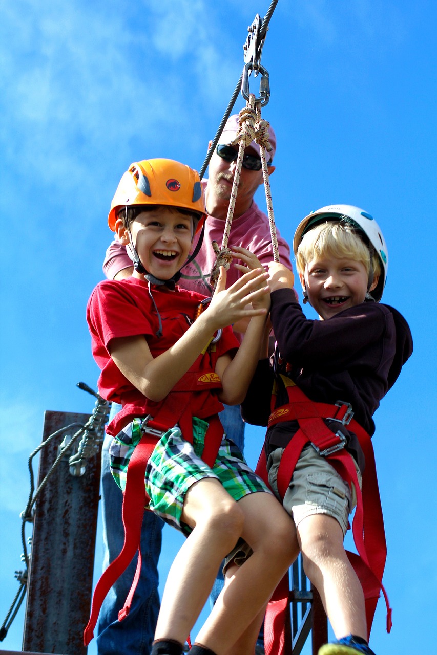 Two smiling children in helmets and harnesses getting ready for a zipline adventure.