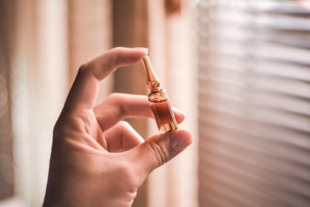 Closeup of a hand holding an ampoule under the sunlight with a window