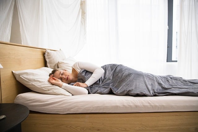 A woman lying on a mattress covered in a light blanket.