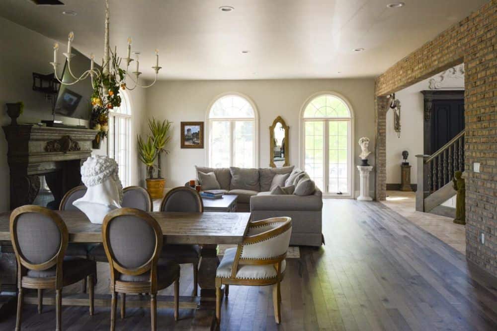 The dining area offers a candle chandelier, round back chairs, and a wooden table topped with a bust sculpture.