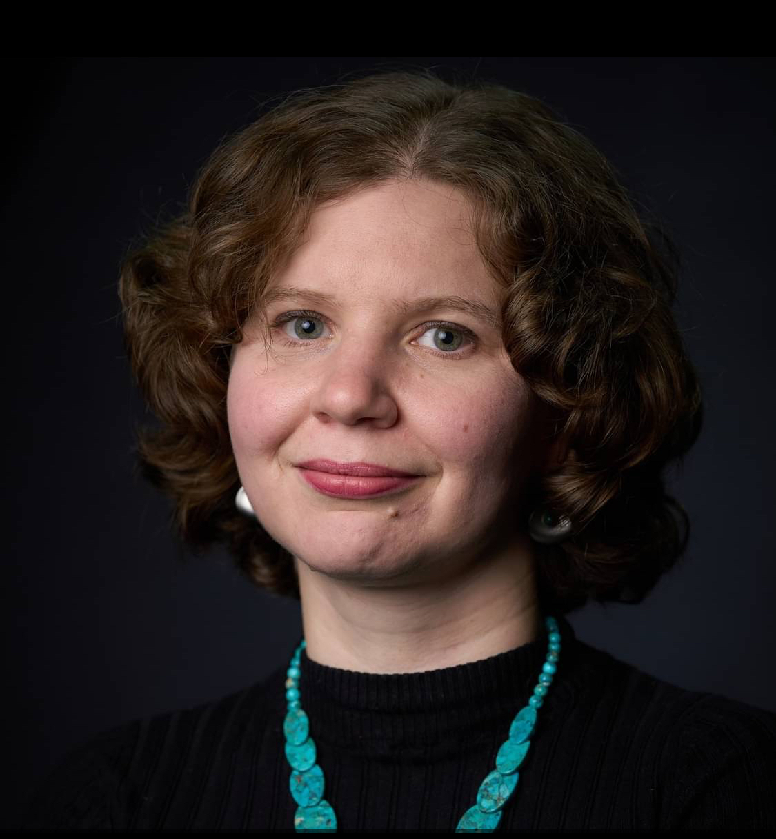 A portrait of a woman wearing a turquoise necklace. Black background.  