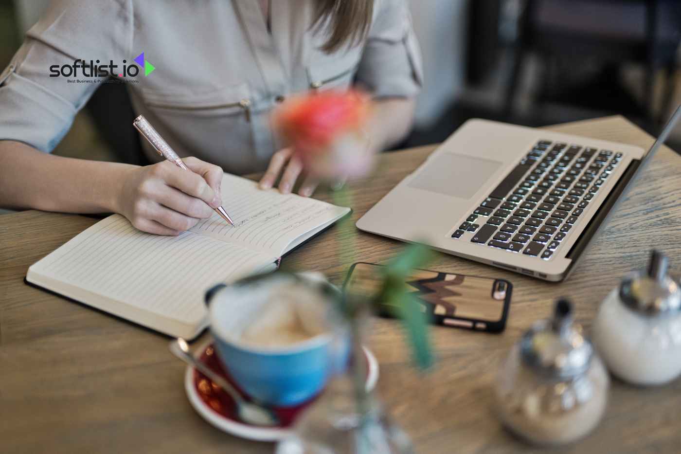 a woman writing on a notebook with a laptop