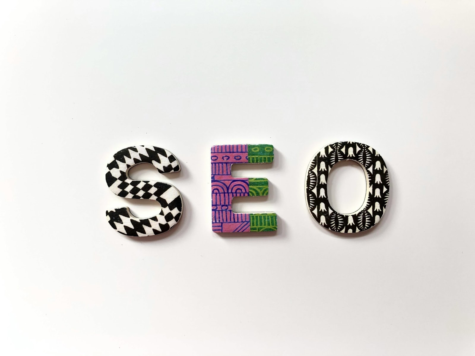 The image shows the letters "SEO" in a playful design with colorful patterns on a white background. 