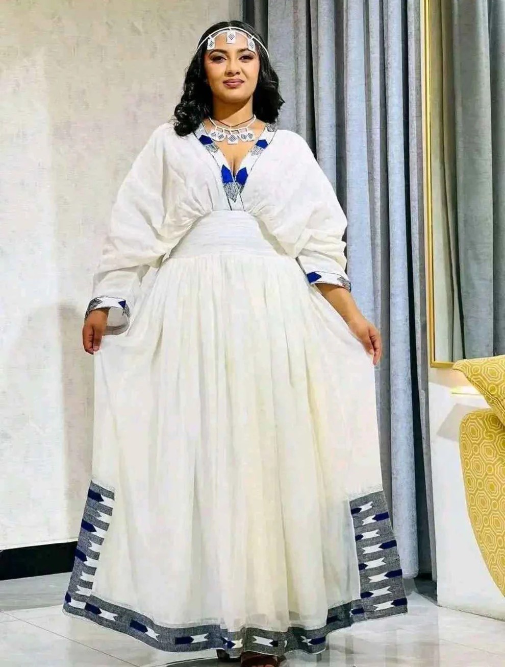 Woman in elegant white formal habesha dress adorned with blue and silver embroidery