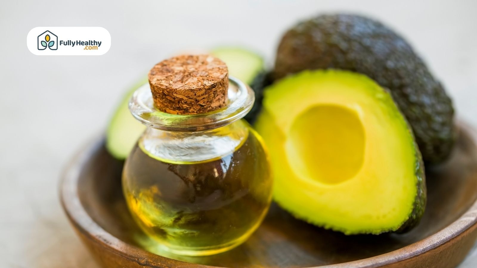 Small glass bottle of avocado oil beside sliced ripe avocado