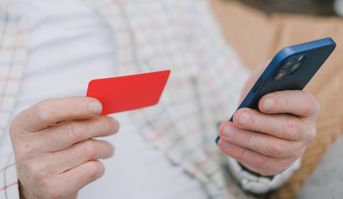 Person holding a red card in one hand and an iPhone in the other