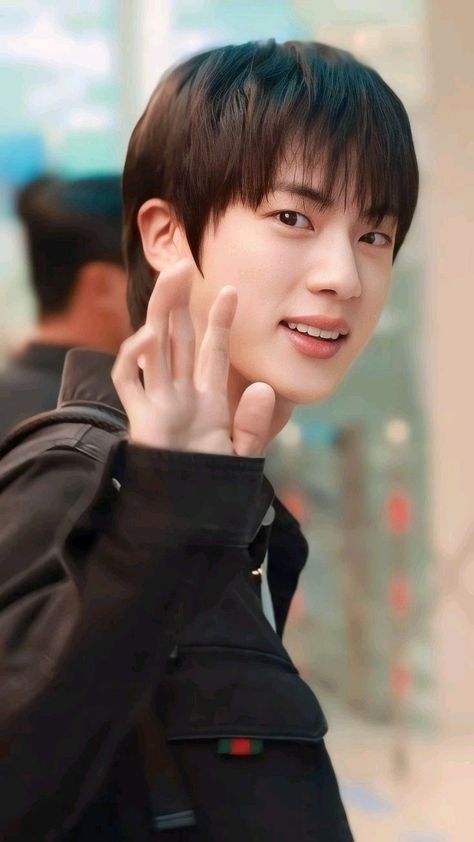 A picture of BST Jin on a black jacket waving his hand 