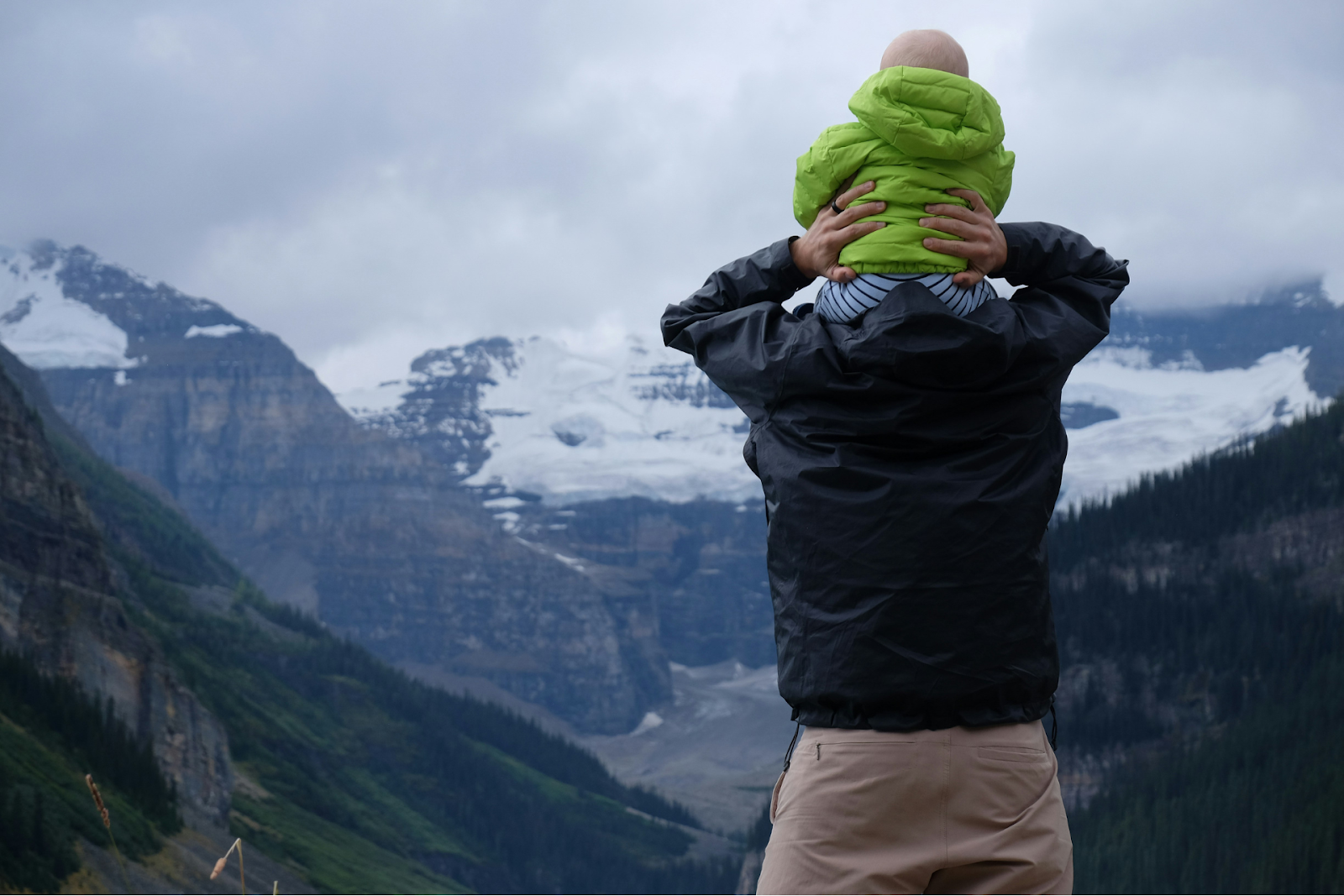 A person holding a baby on their shoulders, looking out at mountains