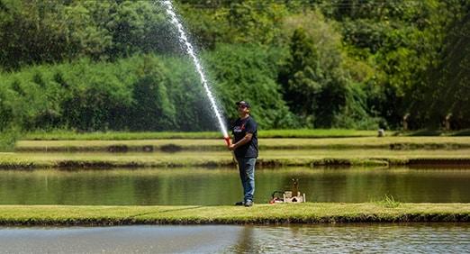 Hombre usando una motobomba Toyama para arrojar agua a un estanque