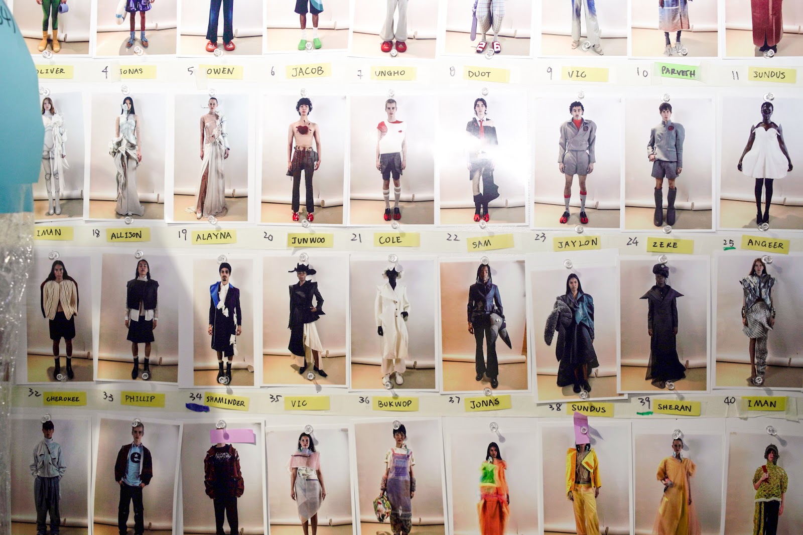 A wall of backstage model polaroids shows looks numbered and labeled with names, displaying various fashion designs.