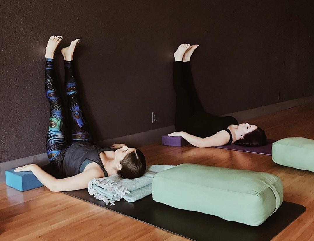 two women are laying down with their feet up the wall, resting in a restorative yoga pose