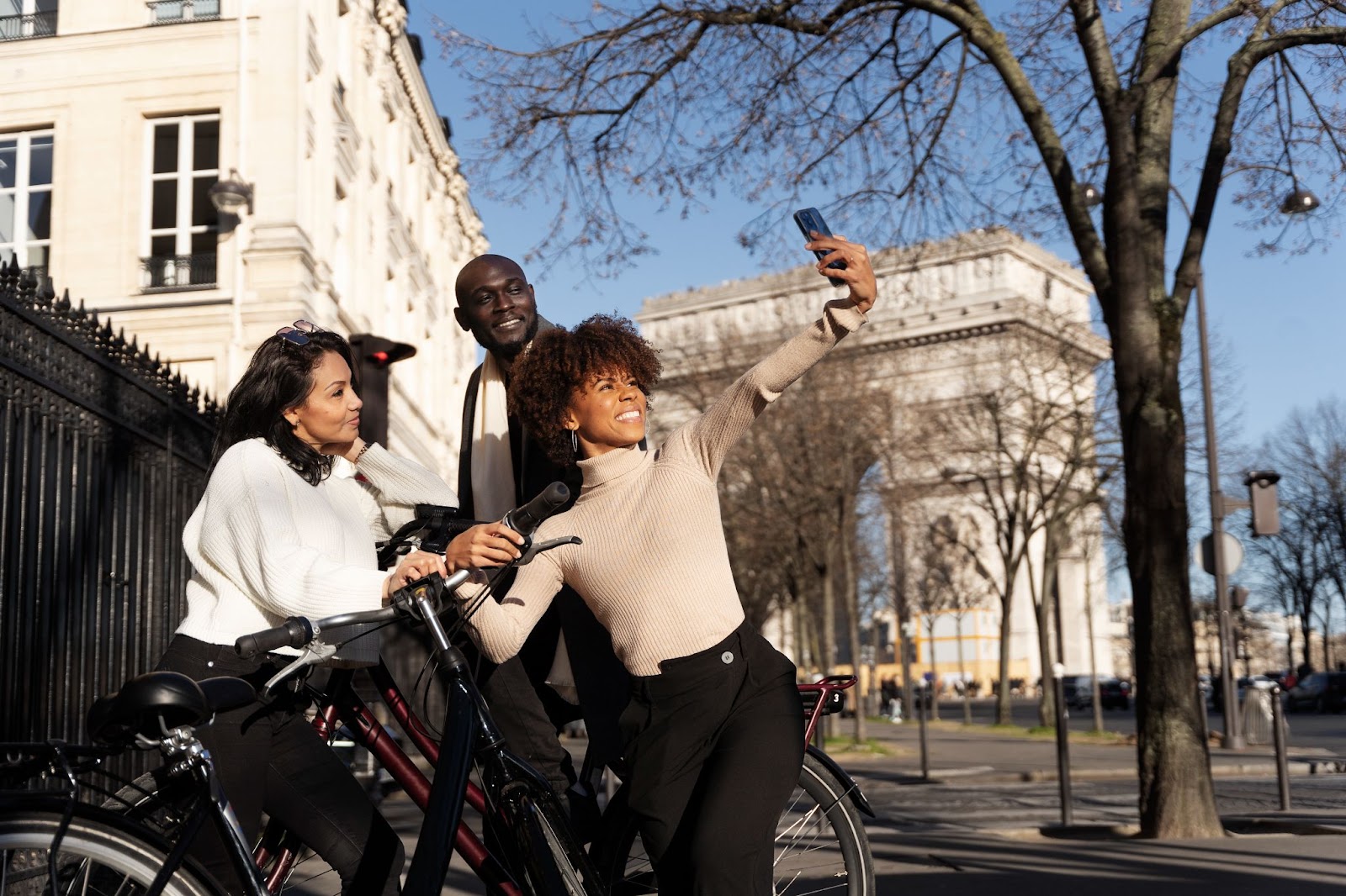 A group of friends taking a break during their guided electric bike tour in Paris to take a photo in front of the Arc de Triomphe.