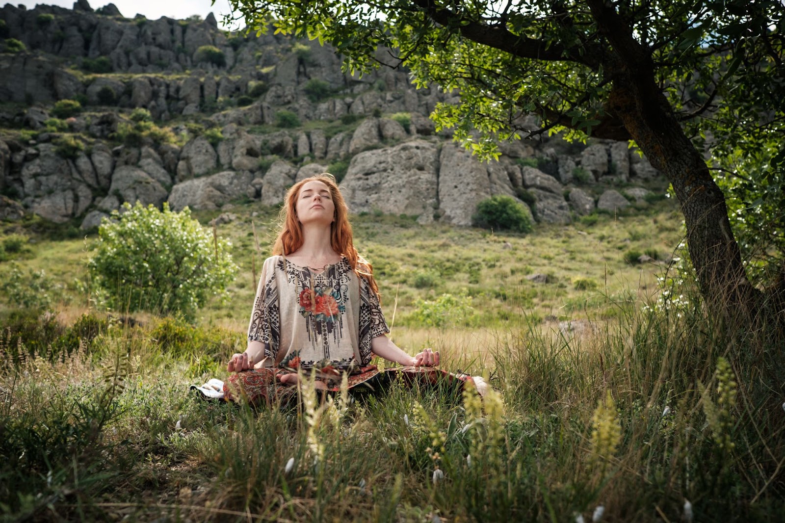 A young girl in a bohemian-inspired outfit meditates in a serene park, embodying the holistic connection between mind, body, and nature.